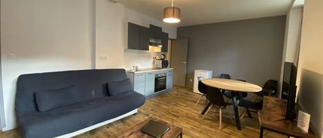 A modern living room with a dark sofa, a wooden coffee table, and a dining area with a table and chairs.