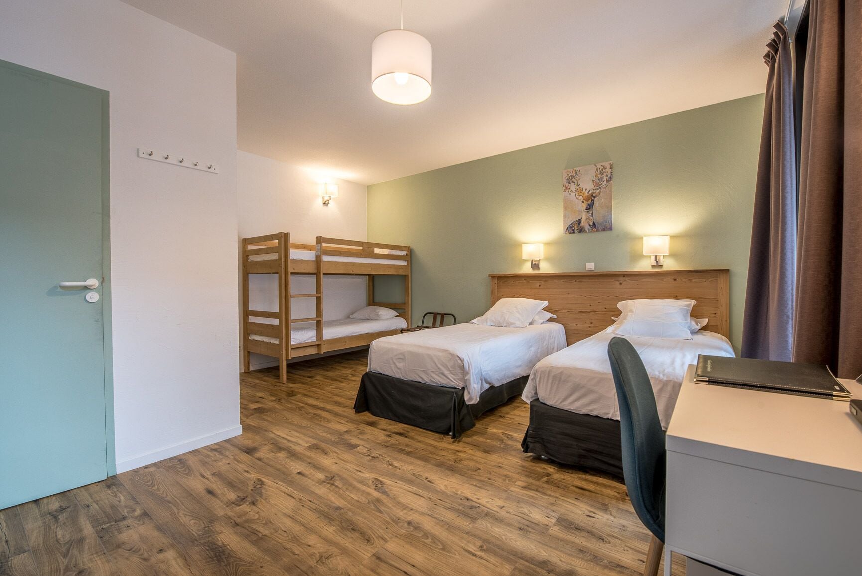 Une chambre avec deux lits simples, un lit superposé, un bureau avec une chaise et une lampe fixée au mur.