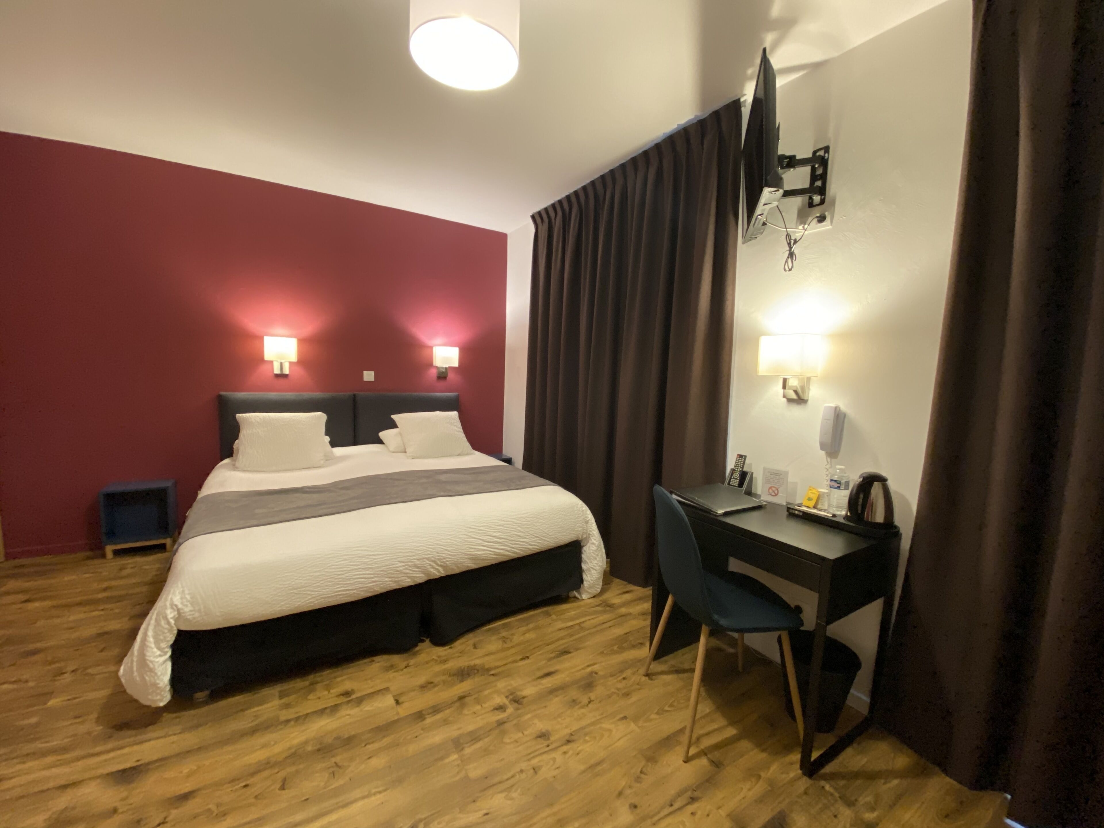 A hotel room with a bed, desk, chair, and a lamp.