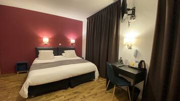 A hotel room with a bed, desk, chair, and a lamp.