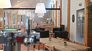 Ein moderner Innenbereich mit Billardtisch, Holztischen und schwarzen Sofas.
