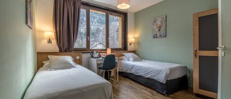 A room with two single beds, a desk, a chair, and a window with curtains.