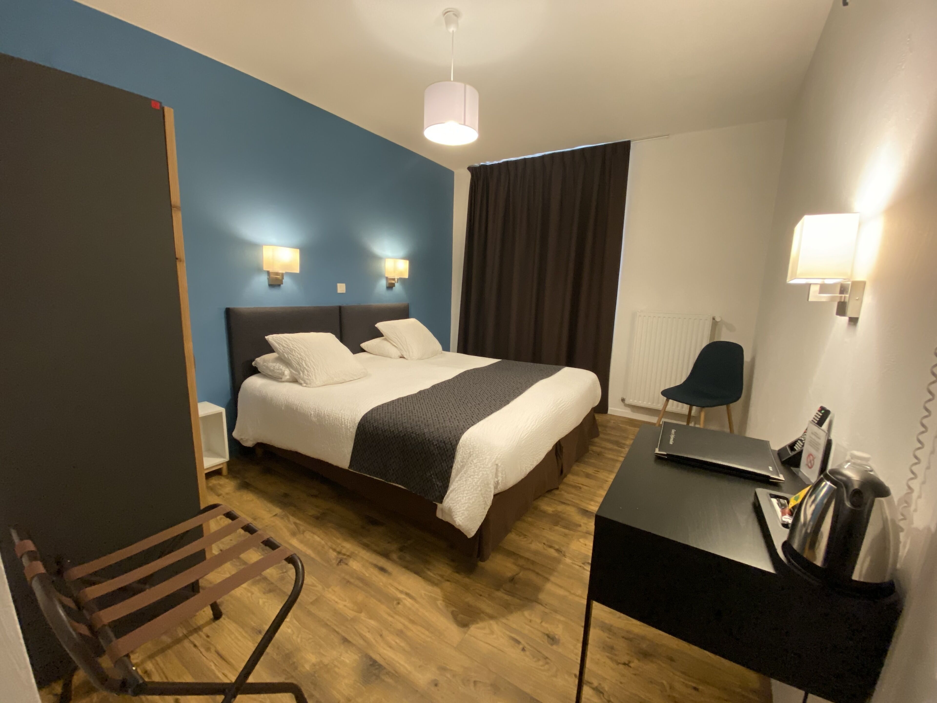 Ett modernt hotellrum med en stor säng, sänglampor, ett skrivbord med en bärbar dator, en stol och ett element.