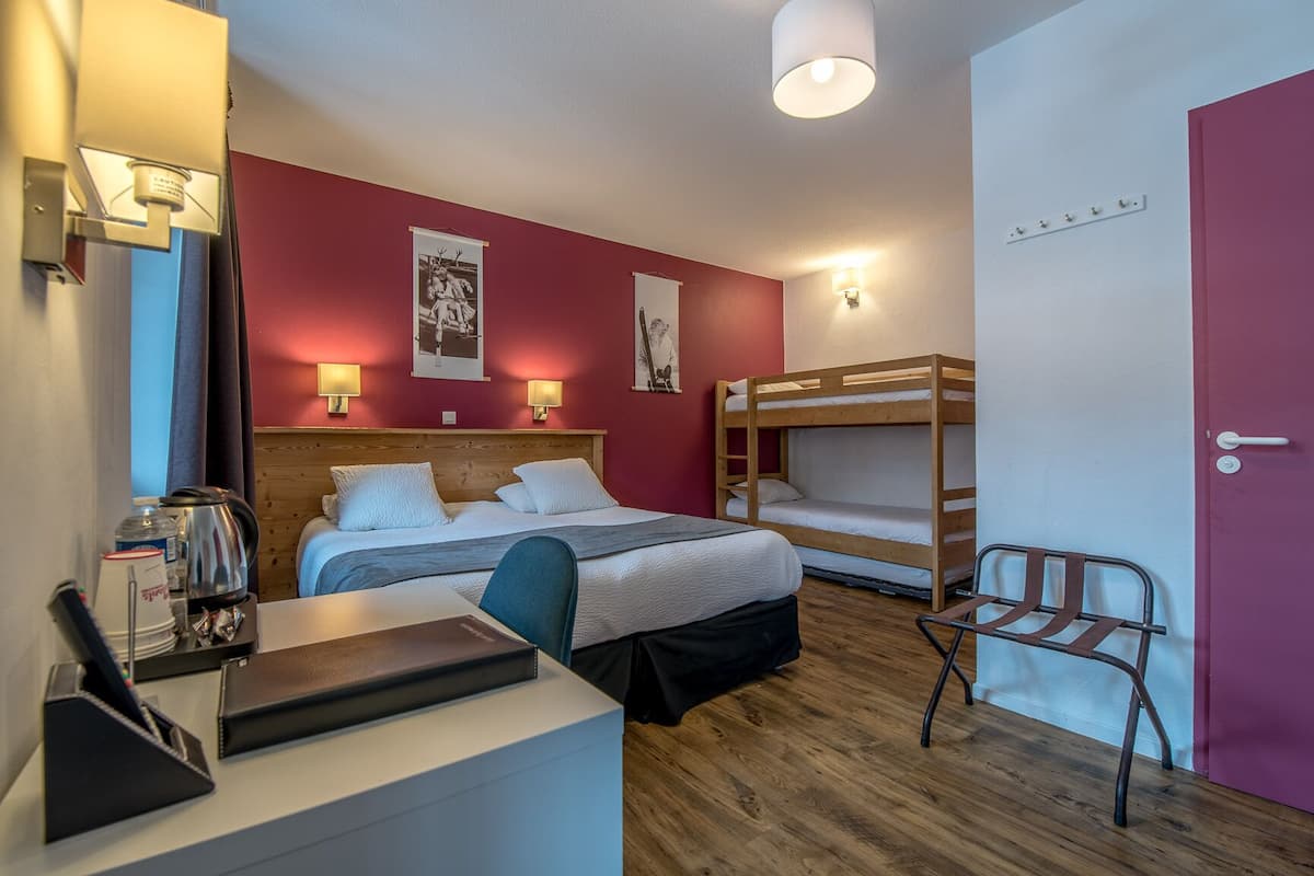 A hotel room with a bunk bed, a desk with a chair, and a small table with a kettle and cups.
