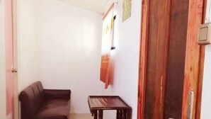 A room with a dark brown sofa, a small wooden table, and a wooden door with a number '2' above it. - Talisay Point Homes (Moalboal)
