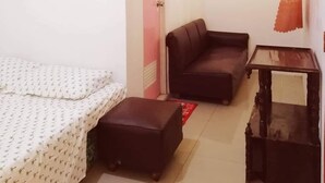 A small, well-lit room with a bed, a sofa, a small table, and a door. - Talisay Point Homes (Moalboal)