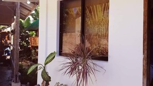 A single-story building with a white exterior and a corrugated metal roof. There is a window with a view of a plant and a thatched structure in the background. - Talisay Point Homes (Moalboal)