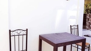 A small outdoor patio with a table and two chairs, a window with a floral view, and a concrete floor. - Talisay Point Homes (Moalboal)