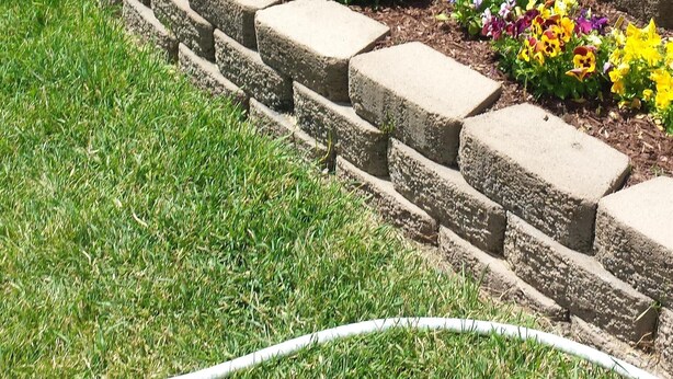 Un jardín ajardinado con un muro de piedra, diversas plantas florecientes y una pequeña estatua de jardín.