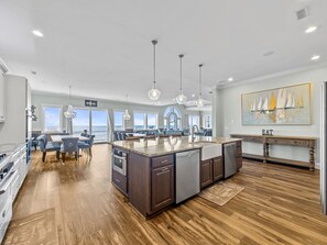Una cocina amplia con una isla grande, iluminación colgante moderna y vista al océano.