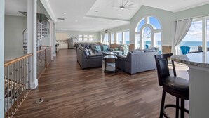 A spacious living area with a large sofa set, a dining table, and a kitchen in the background. - Experience oceanfront luxury at Topsail Manor, a spacious 8-bedroom paradise in North Topsail Beach. (North Topsail Beach)