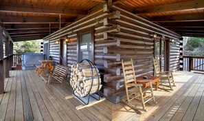 A log cabin with a wooden deck, a hot tub, and wooden rocking chairs.