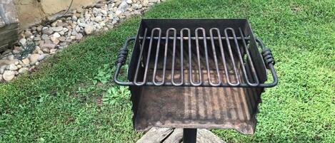 A metal grill with a wooden base, set on a grassy lawn with a stone border and a wooden fence in the background.