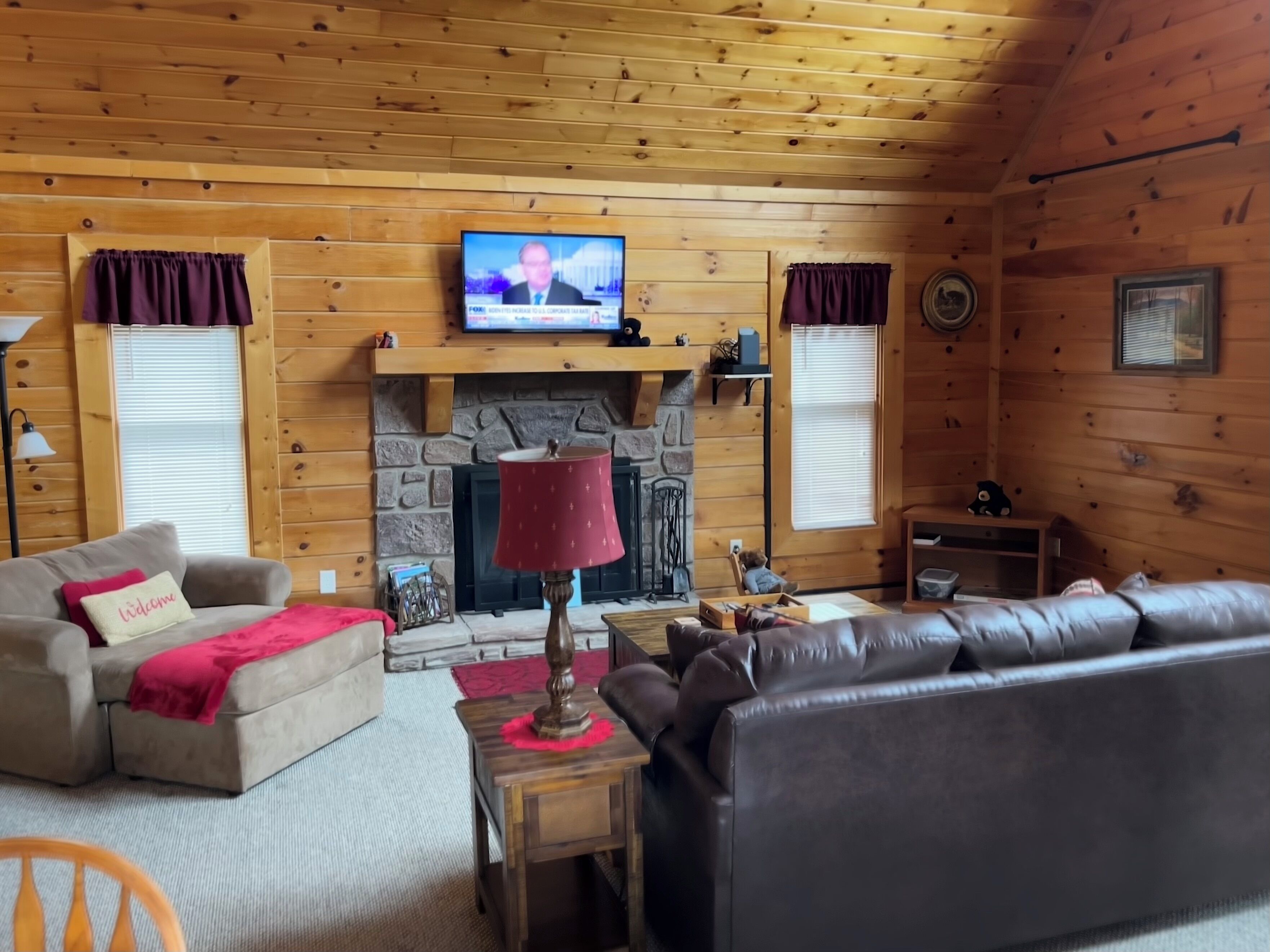 A cozy cabin interior with a stone fireplace, wooden walls, a television, and a leather sofa.