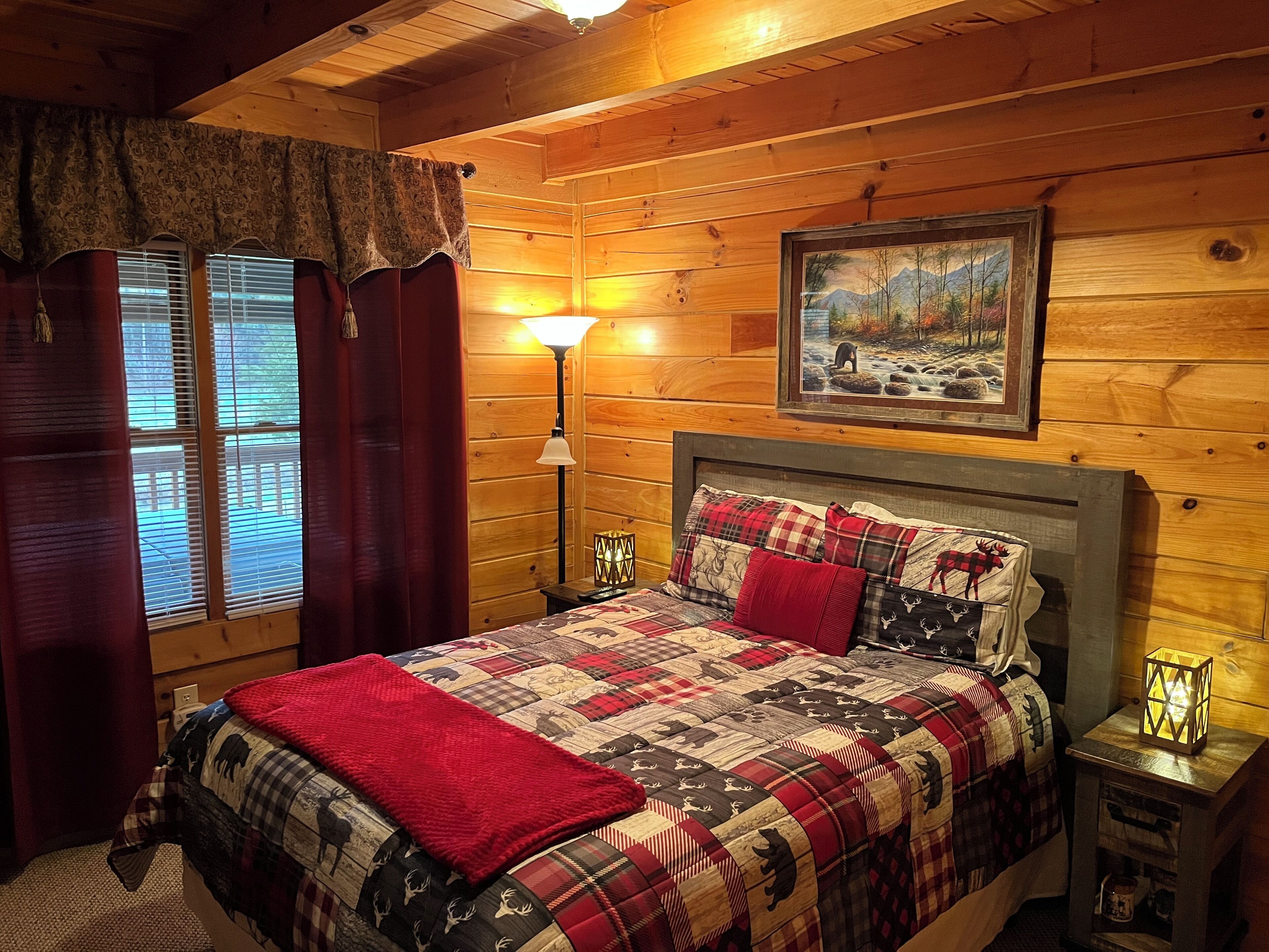 Un dormitorio rústico de cabaña con una cama grande, un cuadro en la pared y una ventana con cortinas.