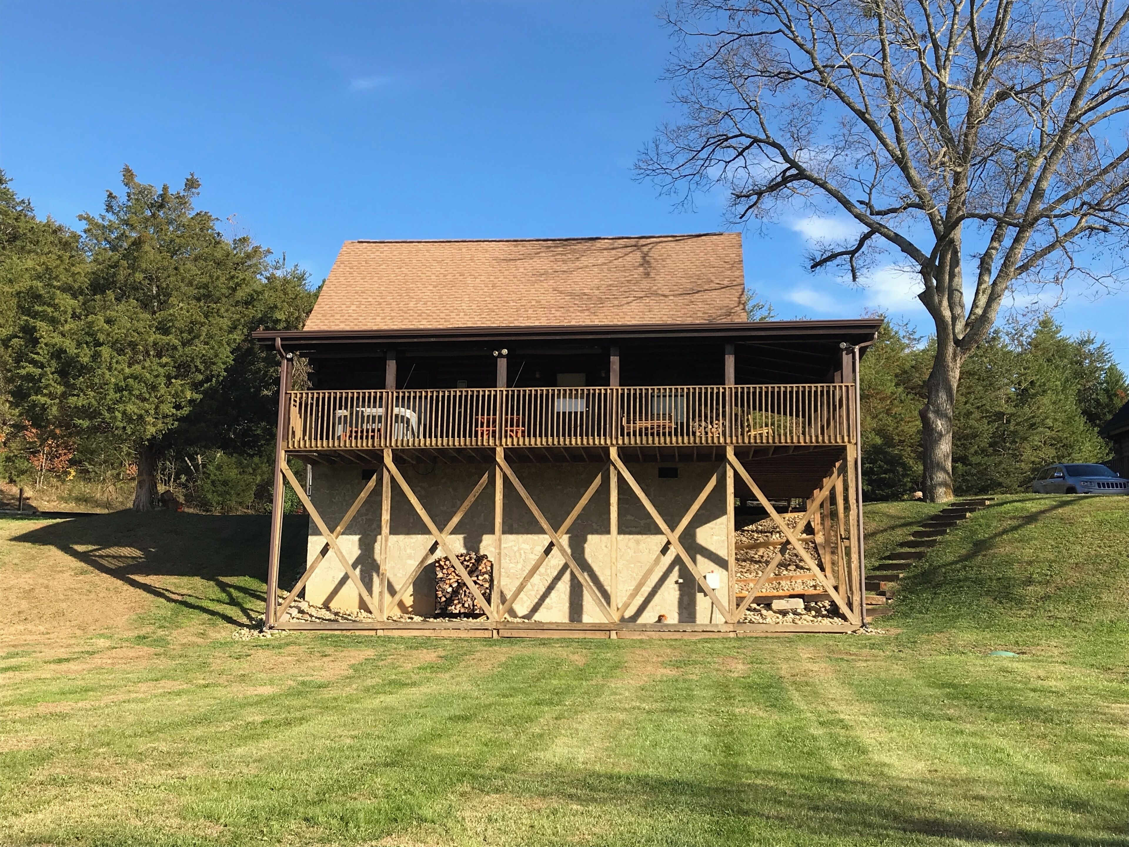 A wooden cabin with a balcony, surrounded by trees and a grassy area.