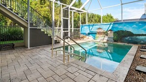 En indendørs swimmingpool med et glasomkranset område, en trappe og et muralmaleri på væggen.