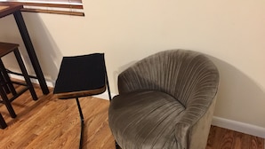 A corner room with a dark grey upholstered armchair, a small black side table, and a wooden floor. - HUGE UPDATED & CLEAN Studio Apartment, Downtown & Beaches Nearby!  (St. Petersburg)