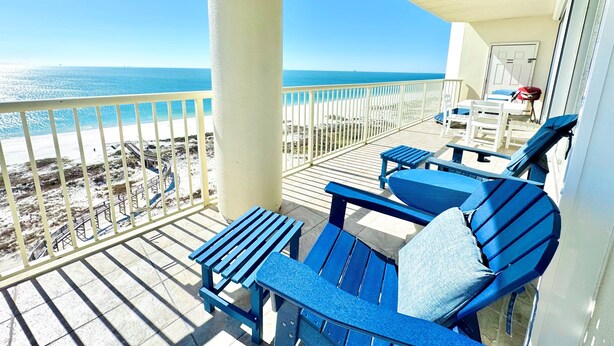 A balcony with a view of the beach, blue chairs, and a table. - Beach Club Corner Unit! Direct Gulf View - Pools - Beach - Grill -Upgraded Cable (Gulf Shores)