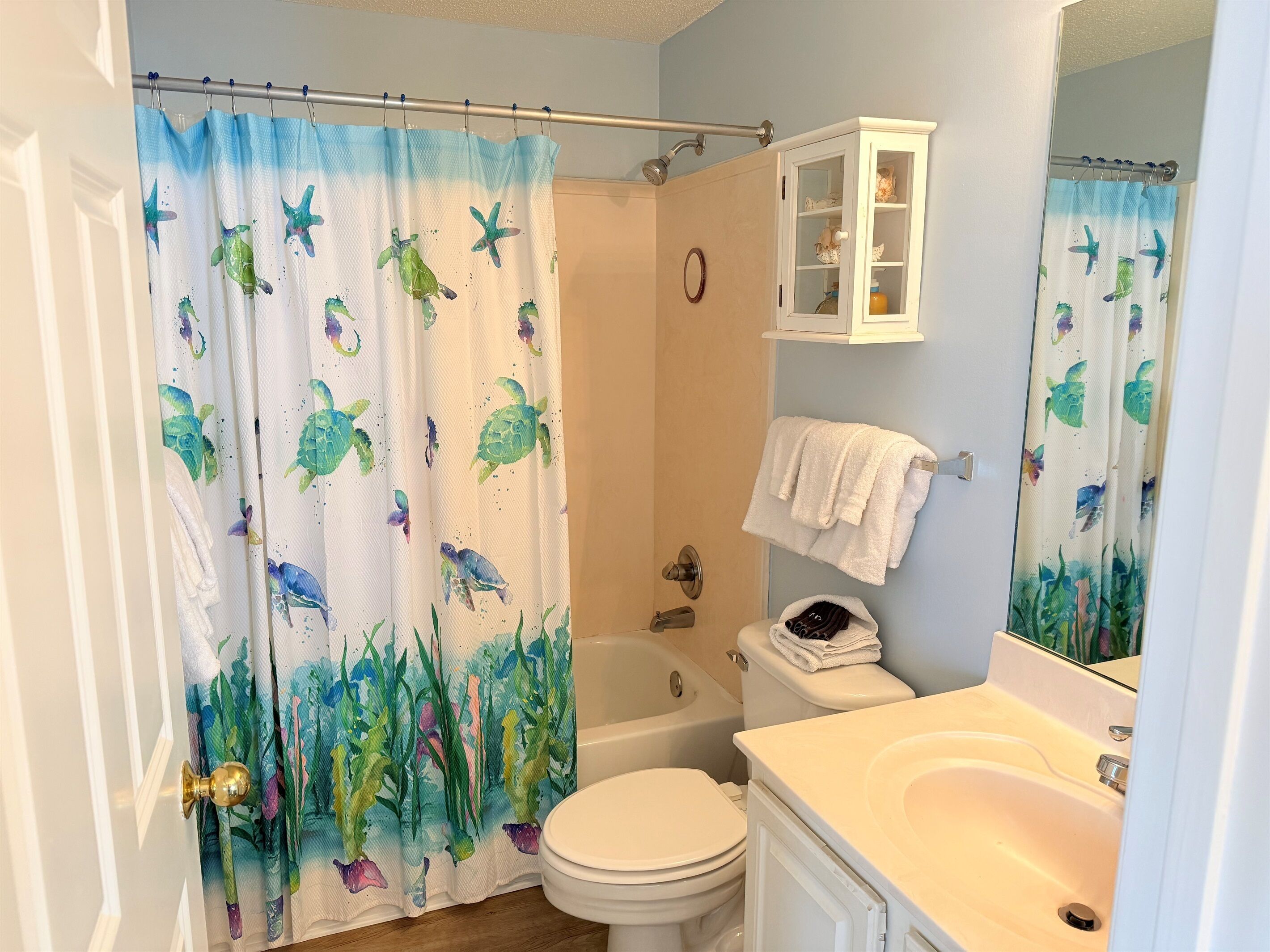A bathroom with a shower curtain featuring sea creatures, a bathtub, a toilet, a sink, and a cabinet with toiletries.