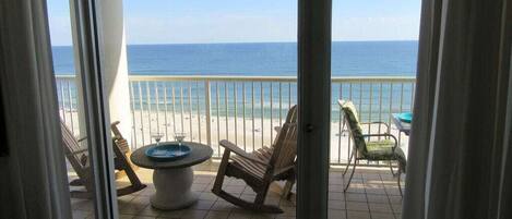 A balcony with a view of the ocean, a table, and several chairs.