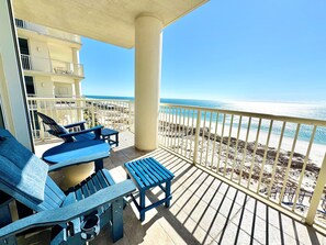 Un balcón con mobiliario azul, vista a la playa y un edificio con balcones.