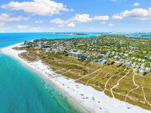 An aerial view of a coastal area with a beach, residential buildings, and a marina.