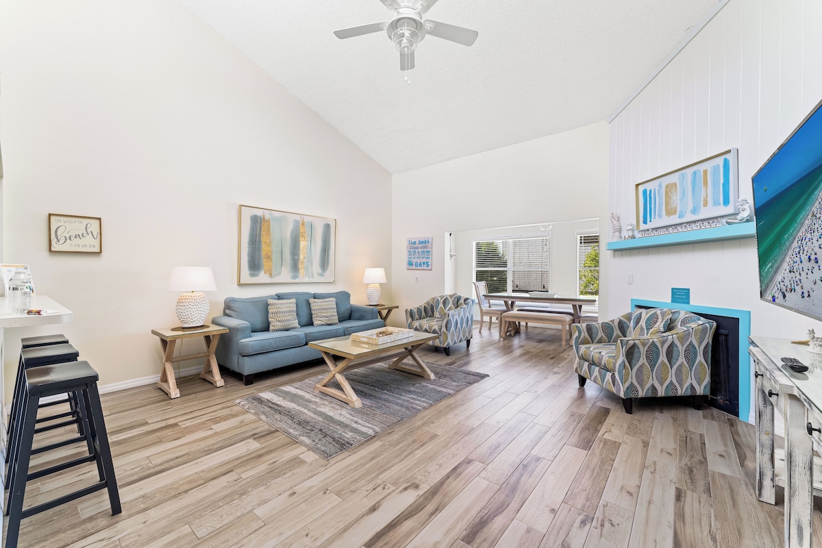 A spacious living area with a blue sofa, a patterned armchair, a wooden coffee table, and a ceiling fan.