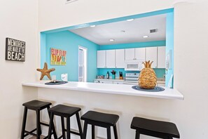 A kitchen with a teal accent wall, white cabinets, and a central island with stools. - Living the Dream by Beachside Managment (Siesta Key)