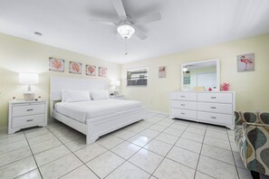 Un dormitorio con cama, mesitas de noche, cómoda, ventilador de techo y decoración en las paredes.