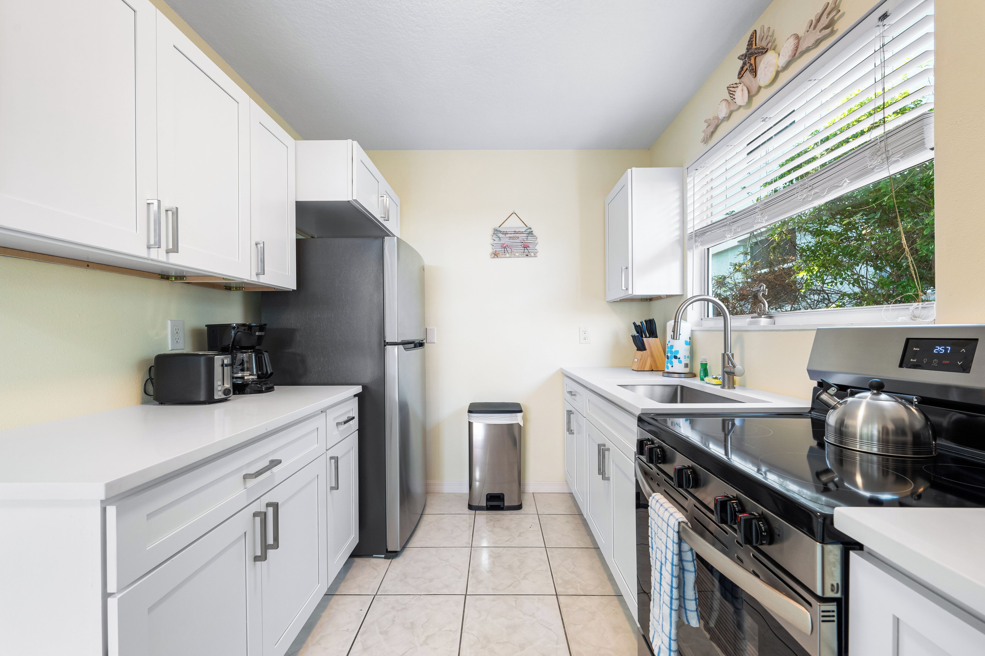A modern kitchen with white cabinets, stainless steel appliances, and a window with blinds.