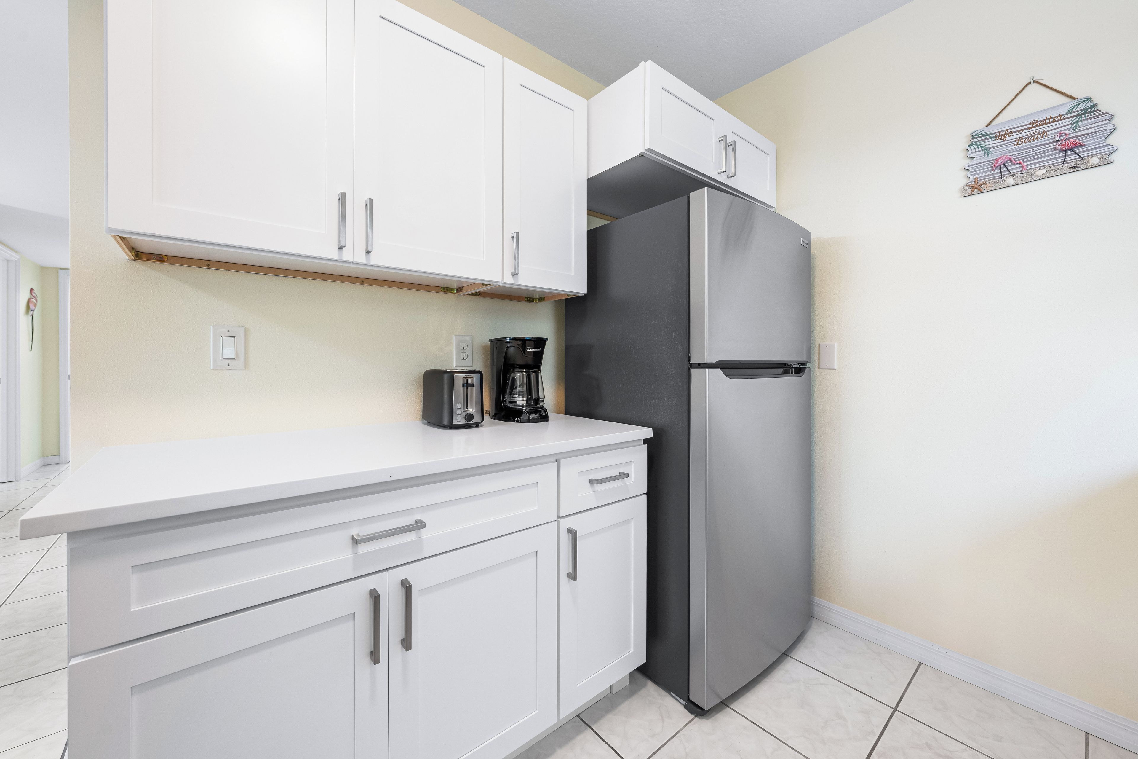 A kitchen with white cabinets, a stainless steel refrigerator, and a coffee maker on the counter.