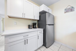 Una cocina con armarios blancos, un refrigerador de acero inoxidable y una cafetera en la encimera.