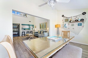 Una sala de estar moderna con una mesa de comedor de vidrio, un sofá y una zona de cocina al fondo.
