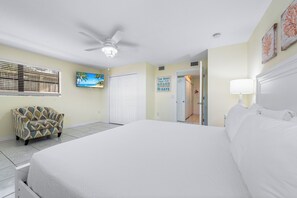 A bedroom with a large bed, a ceiling fan, a TV, and a door leading to another room. - Living the Dream by Beachside Managment (Siesta Key)