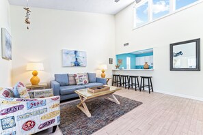A modern living room with a sofa, coffee table, and a kitchen area with bar stools.