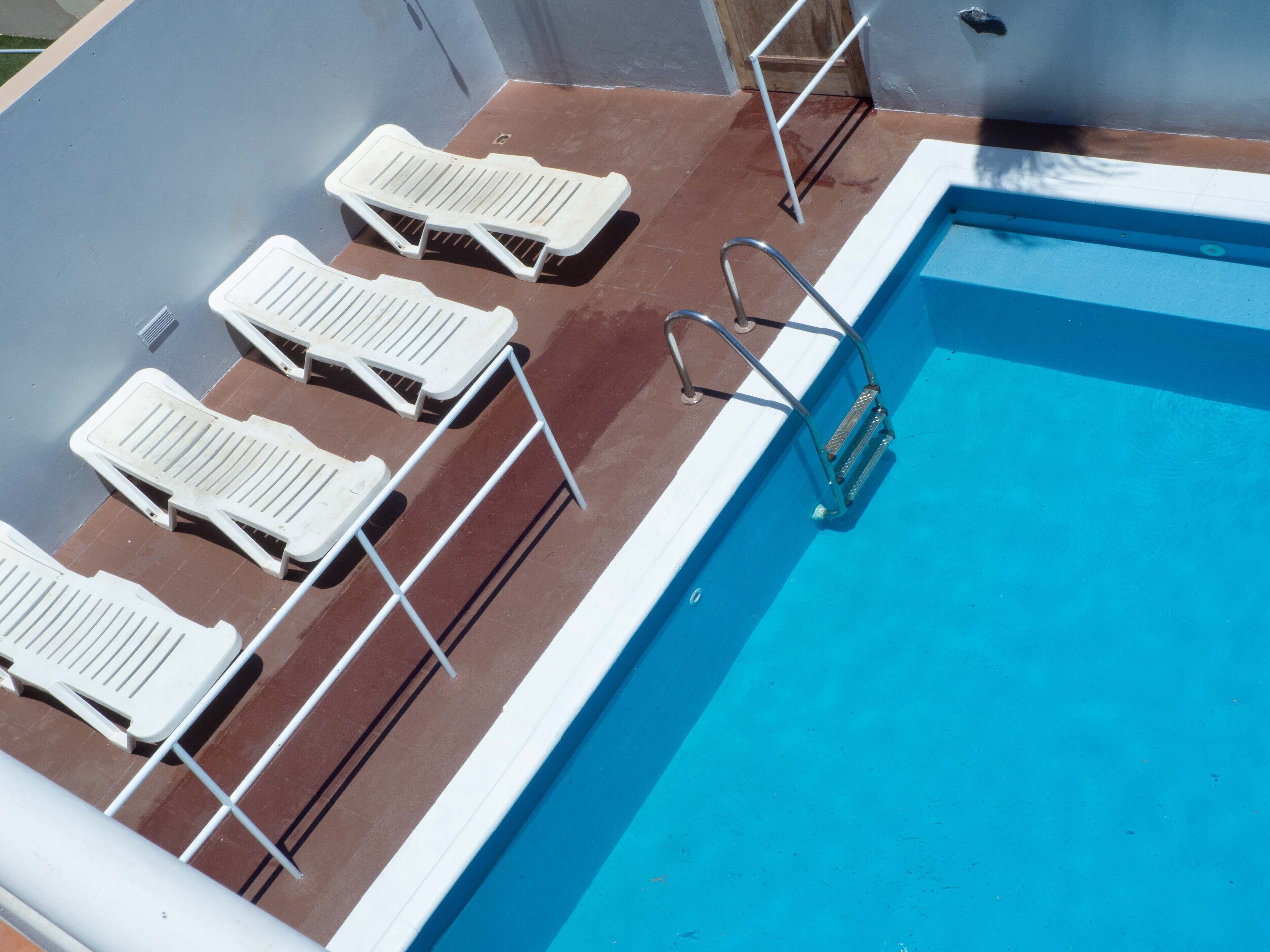 Zona de piscina con sillas reclinables blancas y una escalera de acceso.