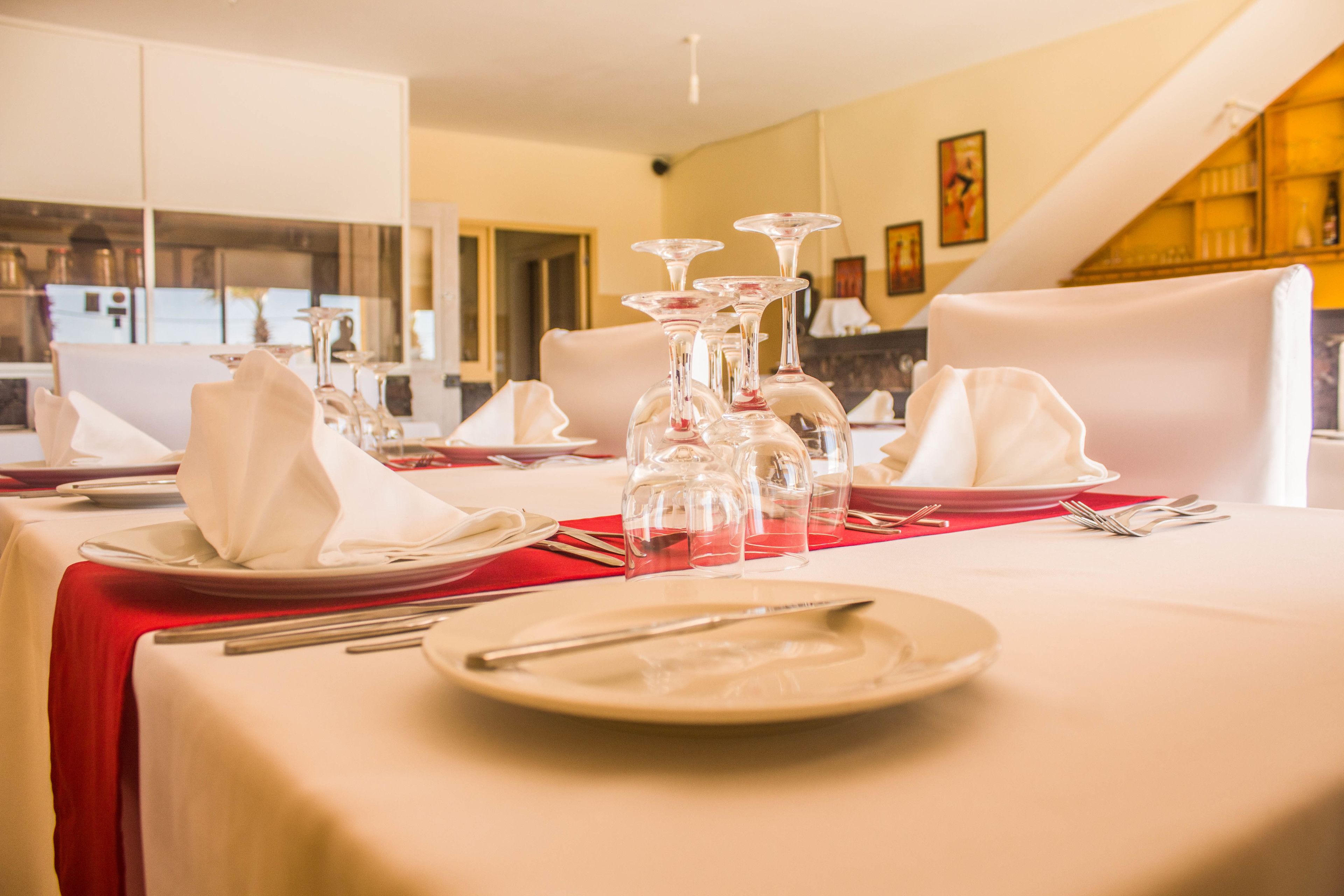 A dining table set with white plates, napkins, and clear wine glasses, with a red tablecloth.