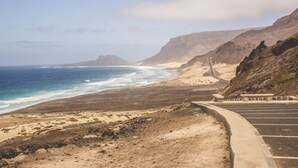 A coastal road with a parking area and a view of the ocean and mountains. - Restaurante Baia Guest House (São Vicente)