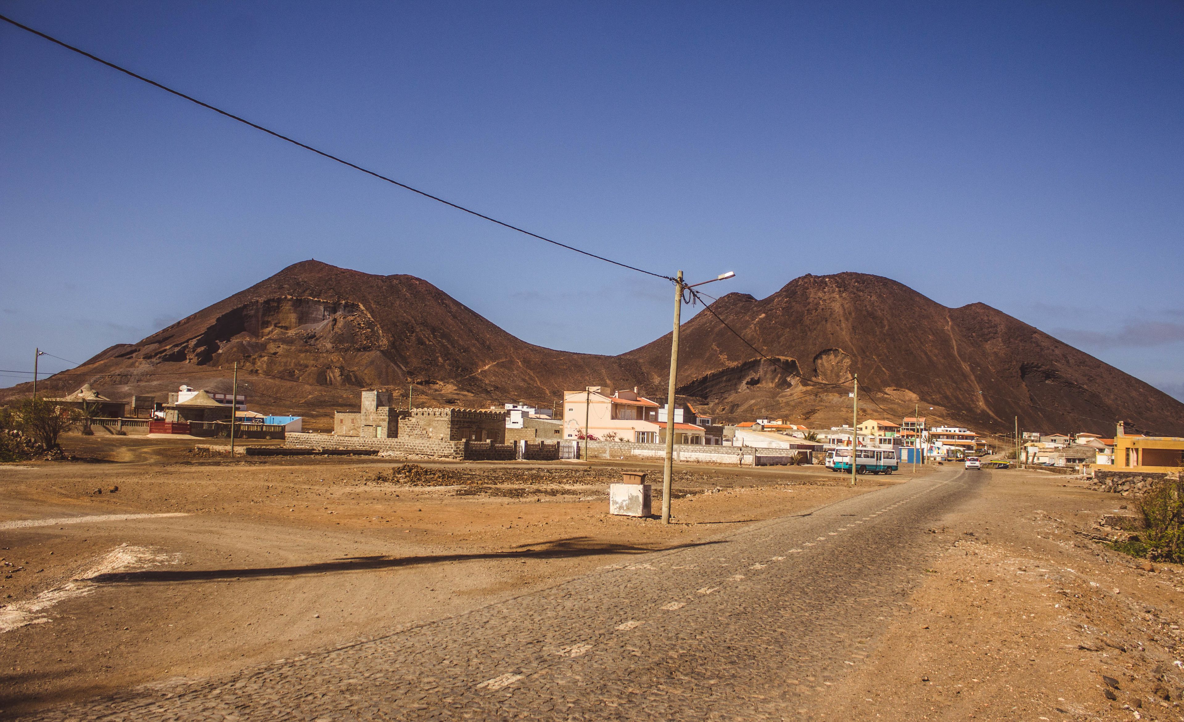A rural road with buildings and a mountain in the background.