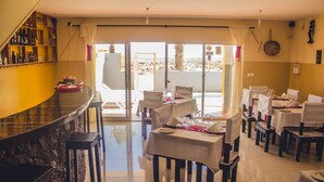 A restaurant with a bar area, multiple tables set for dining, and a view of the outdoors. - Restaurante Baia Guest House (São Vicente)
