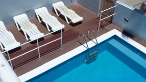 A poolside area with white lounge chairs and a metal ladder leading into the pool. - Restaurante Baia Guest House (São Vicente)