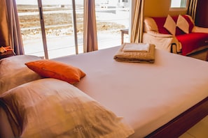 A hotel room with a bed, pillows, and a view of the beach through large windows. - Restaurante Baia Guest House (São Vicente)