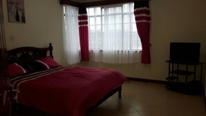 Ein Schlafzimmer mit Bett, Fernseher und einem Fenster mit Vorhängen.