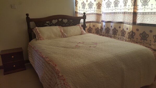 A bed with a wooden headboard, a quilted white bedspread, and floral-patterned curtains.