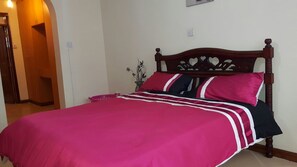 A bed with a wooden headboard, a pink bedspread, and two pillows.