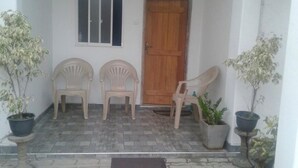 Eine Veranda mit drei Plastikstühlen, einer Holztür und Topfpflanzen.