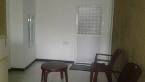 Ein Zimmer mit einer weißen Tür, einem Fenster mit einem gemusterten Rollo, einem Holzstuhl und einem kleinen runden Tisch.