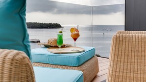 A balcony with wicker furniture, a view of the sea, and two drinks on a tray. - Hotel Valsabbion (Medulin)
