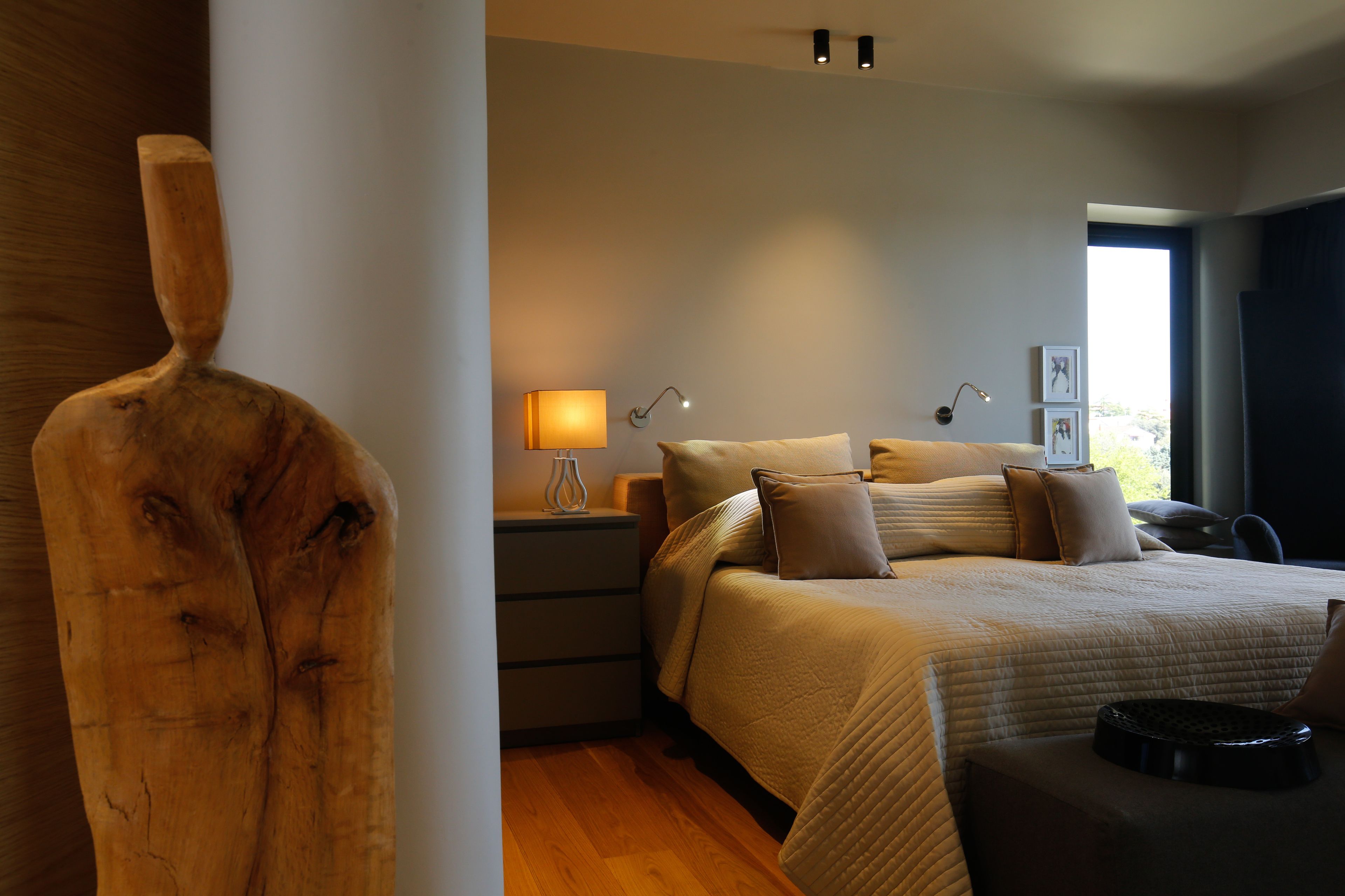 A modern bedroom with a large bed, bedside lamps, and a wooden sculpture.